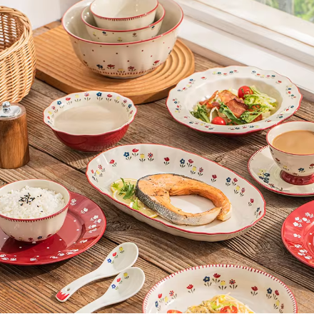 Set of ceramic dishes with floral patterns on a wooden table by a window.